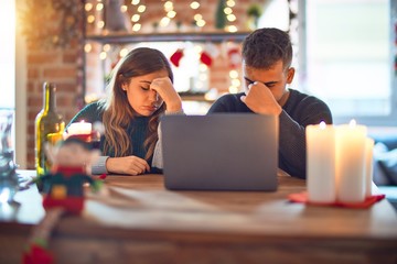 Sticker - Young beautiful couple sitting using laptop around christmas decoration at home tired rubbing nose and eyes feeling fatigue and headache. Stress and frustration concept.