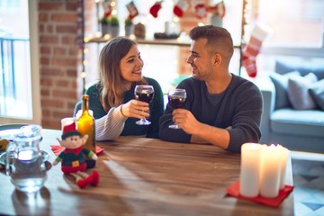 Wall Mural - Young beautiful couple smiling happy and confident. Toasting with cup of wine celebrating christmas at home