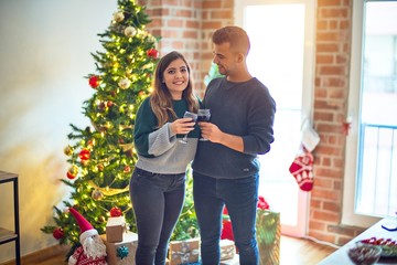 Wall Mural - Young beautiful couple smiling happy and confident. Toasting with cup of wine celebrating christmas at home