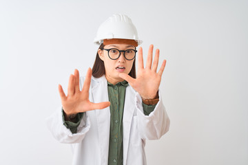 Sticker - Young chinese engineer woman wearing coat helmet glasses over isolated white background afraid and terrified with fear expression stop gesture with hands, shouting in shock. Panic concept.