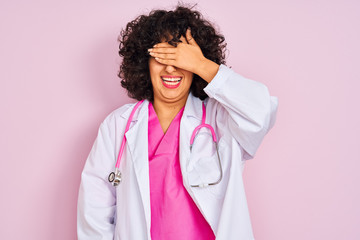 Sticker - Young arab doctor woman with curly hair wearing stethoscope over isolated pink background smiling and laughing with hand on face covering eyes for surprise. Blind concept.