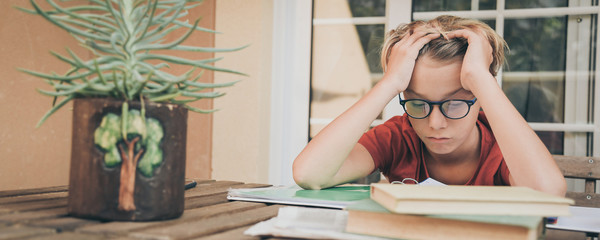 Tired student doing homework at home sitting outdoor with school books and newspaper. Boy weary due to heavy study. Kid asleep on the copybook after long tasks. Youth, education and fatigue concept.