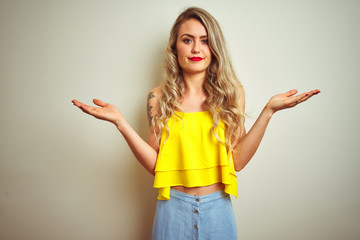 Sticker - Young beautiful woman wearing yellow t-shirt standing over white isolated background clueless and confused expression with arms and hands raised. Doubt concept.