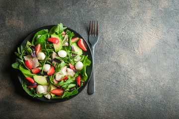 Wall Mural - Salad with fresh strawberries, mozzarella, chicken, avocado and fresh herbs on a dark plate on a dark background.