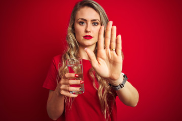 Wall Mural - Young beautiful woman drinking a glass of water over red isolated background with open hand doing stop sign with serious and confident expression, defense gesture