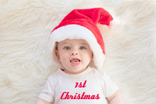 Adorable Baby Boy Wearing Red Santa’s Hat And White T-shirt On A Fluffy Background With Text 1st Christmas