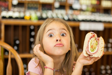 young child makes funny faces while eating a sandwich