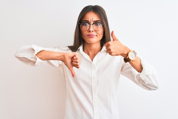Wall Mural - Young beautiful businesswoman wearing glasses standing over isolated white background Doing thumbs up and down, disagreement and agreement expression. Crazy conflict
