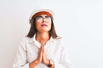 Poster - Young beautiful architect woman wearing helmet and glasses over isolated white background begging and praying with hands together with hope expression on face very emotional and worried. Asking