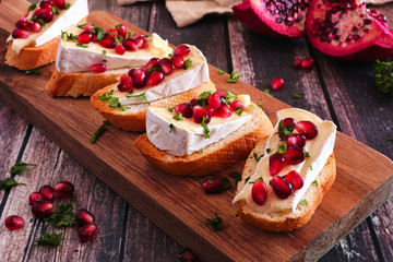 Holiday crostini appetizers with brie cheese, pomegranates and parsley. Close up on a serving board against a rustic wood background. Party food concept.