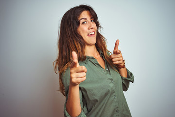 Wall Mural - Young beautiful woman wearing green shirt standing over grey isolated background pointing fingers to camera with happy and funny face. Good energy and vibes.