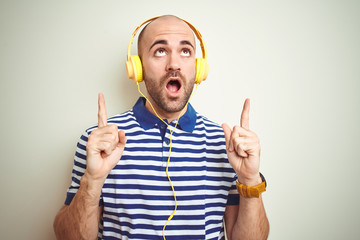 Sticker - Young man listening to music wearing yellow headphones over isolated background amazed and surprised looking up and pointing with fingers and raised arms.