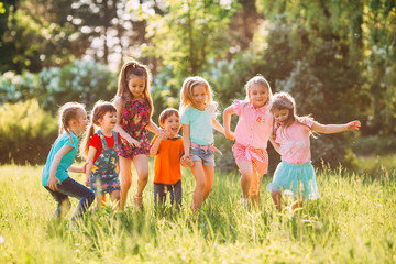 Large group of kids, friends boys and girls running in the park on sunny summer day in casual clothes .