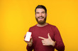 © Vulp - A cheerful bearded guy pointing at mobile, wearing red sweater, winter discount, yellow backgroound