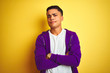 Young brazilian man wearing purple sweatshirt standing over isolated yellow background skeptic and nervous, disapproving expression on face with crossed arms. Negative person.
