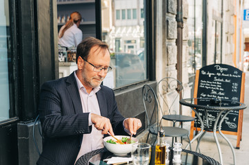 businessman having lunch on a terrace in outdoor cafe, wearing a suit. healthy green salad with salm