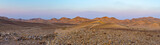 Fototapeta Londyn - Panoramic view of stone desert land with desertic arid mountains and rocks in the background