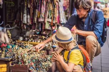 Dad and son at a market in Ubud, Bali. Typical souvenir shop selling souvenirs and handicrafts of Bali at the famous Ubud Market, Indonesia. Balinese market. Souvenirs of wood and crafts of local