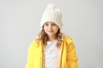 Stylish little girl in winter clothes on light background