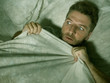  stressed and scared man alone in bed awake at night in fear after having a nightmare feeling paranoid holding the blanket in funny panic face expression