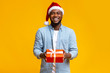 © Prostock-studio - Handsome black guy in red Santa hat holding gift box