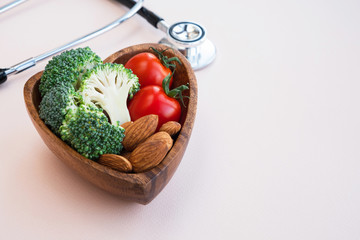 Healthy food for heart on light background. Plate with vegetables, nuts and a medical stethoscope on the table. Diet and medicine concept. Close up, copy space