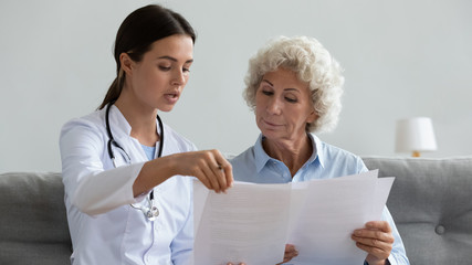 Wall Mural - Serious young doctor explain insurance contract to elder grandma patient