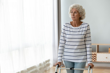 Wall Mural - Thoughtful sad injured old woman standing alone using walking frame