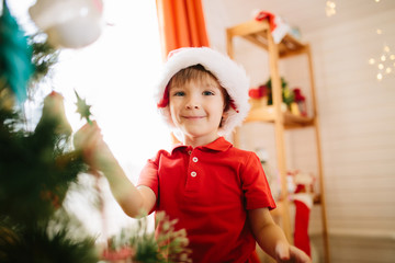 Wall Mural - Cute little boy of about five year with blue eyes decorating a Christmas tree.