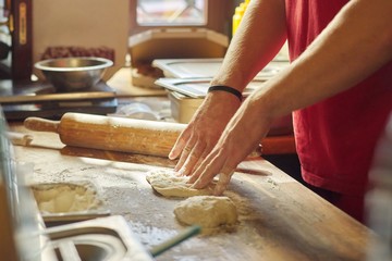 Hands of male baker with flour dough preparing food on wooden table