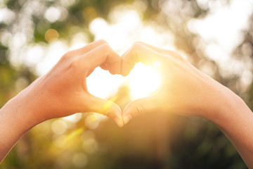 Female hands heart shape on nature bokeh sun light flare and blur leaf abstract background.