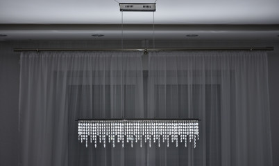 Wall Mural - Rectangle chandelier with hanging crystals with led lighting on the background of a window curtain