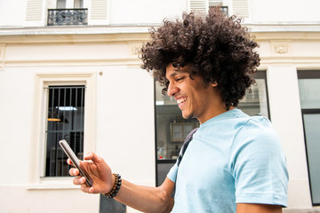 Side of happy young arab man walking and looking at cellphone