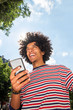 © mimagephotos - happy young north African man holding mobile phone outside and laughing