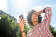 © mimagephotos - happy young north African man holding mobile phone outside and laughing with hand in hair