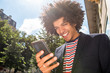 © mimagephotos - Close up smiling young arab guy with afro hair looking at mobile phone outside