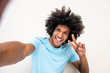 © mimagephotos - happy young North African man taking selfie against white background with peace hand sign