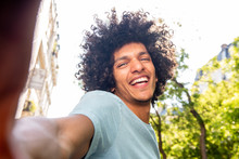 Smiling Young North African Man With Afro Hair Taking Selfie Outside In City