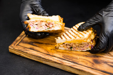 Culinary master class. Closeup of chef hands holding a half of pulled pork sandwich with cheese over wooden board.