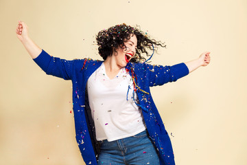 Young laughing woman in confetti celebrates. Yellow background.