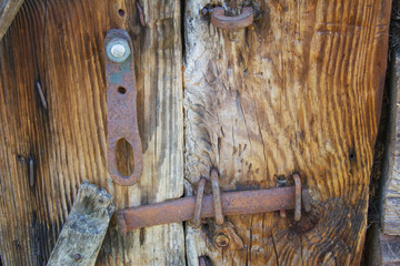 Old lock and a rusty vintage door handle on a peeling painted wooden door that is rotting and weathered on a abandoned building.