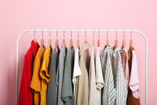 Fashionable Clothes On Hangers On A Wardrobe Rack On A Colored Background.