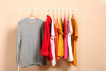 fashionable clothes on hangers on a wardrobe rack on a colored background.