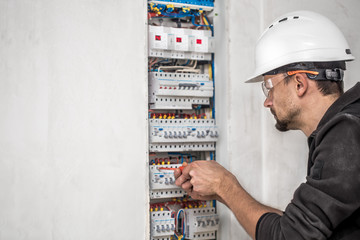 Wall Mural - Man, an electrical technician working in a switchboard with fuses. Installation and connection of electrical equipment.