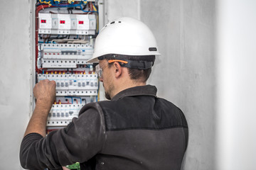 Wall Mural - Man, an electrical technician working in a switchboard with fuses. Installation and connection of electrical equipment.