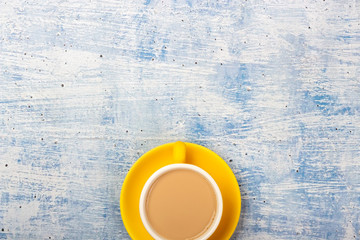 Yellow vivid cup of coffee on blue rustic backdround. Minimal flat lay.