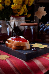 Wall Mural - Grape jelly on a piece of white bread and in glass jars on the wooden board. Autumn still life