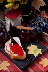 Wall Mural - Grape jelly on a piece of white bread and in glass jars on the wooden board. Autumn still life