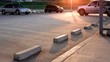 Concrete wheel stops with empty space and three cars parked in outdoor parking lot area with flare light in evening time