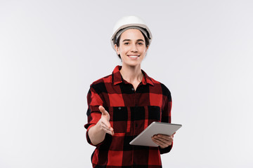 Happy young female architect in hardhat and flannel welcoming you by handshake